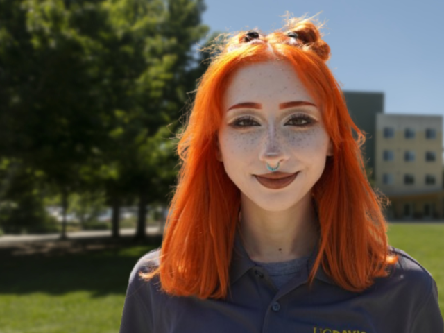 Red-haired woman with freckles smiling in UC Davis polo, sunny campus photograph