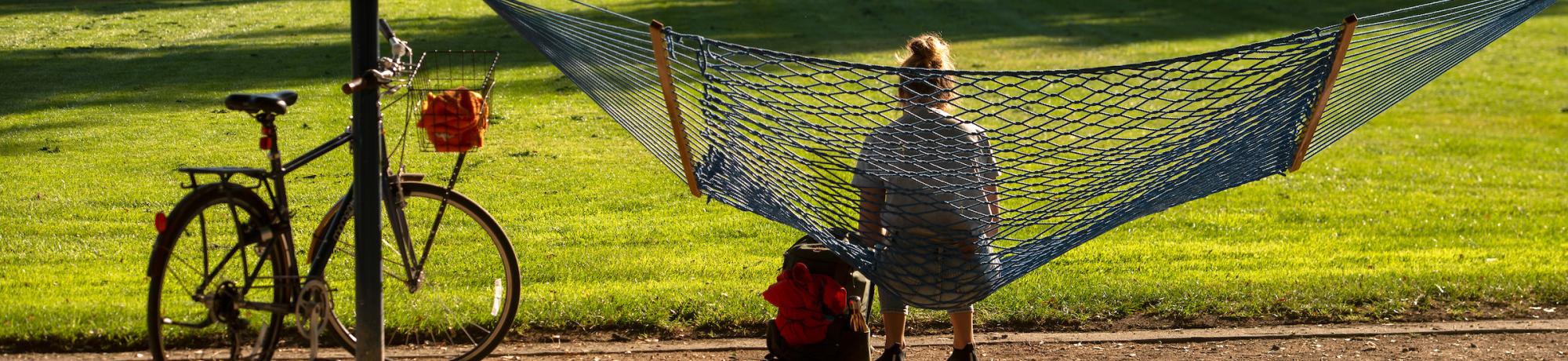 A student sits in a blue hammock with their bike next to them.