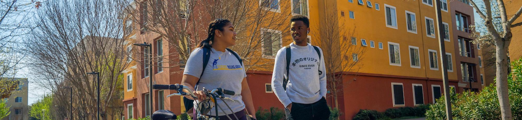 Two students walk with a bike outside the Tercero residence halls.