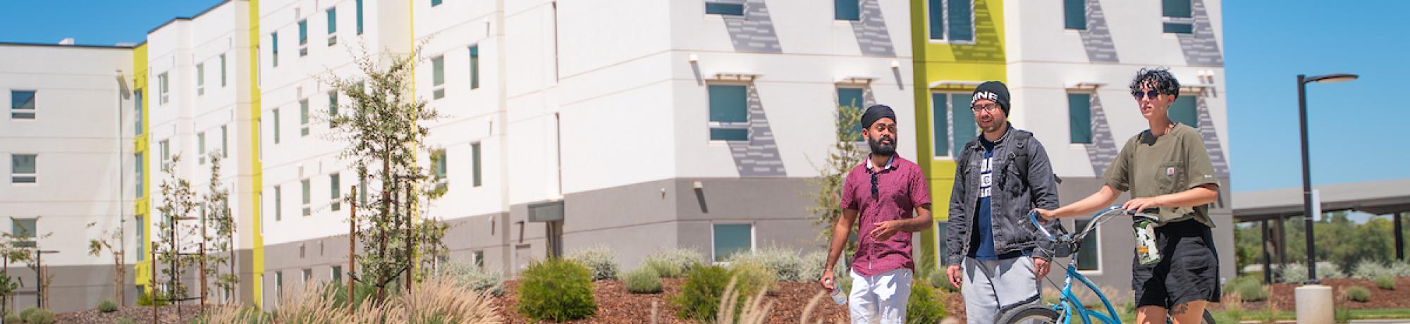 Three students walk with a bike outside the Green residence halls.